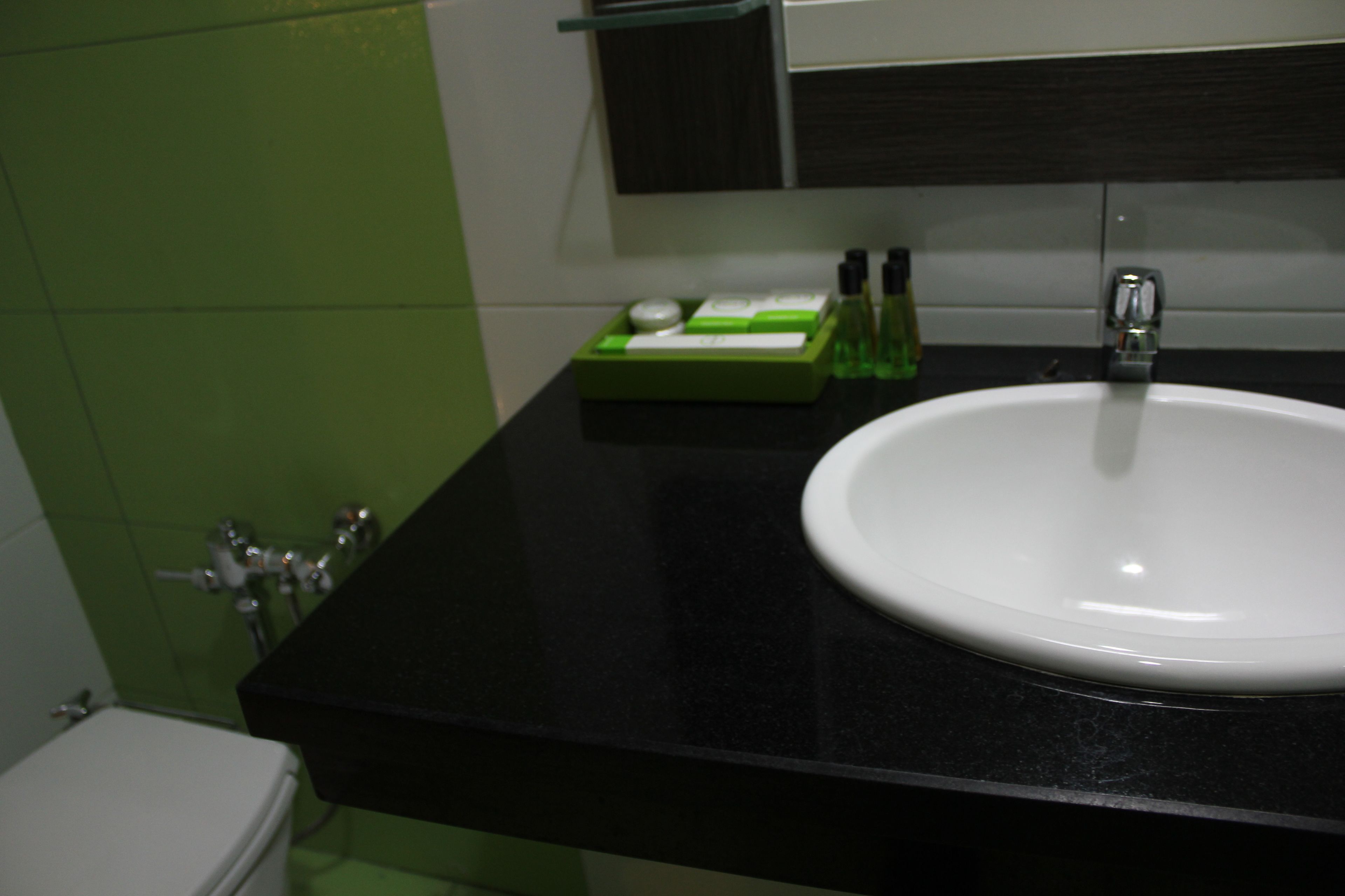 A bathroom with a white sink, black countertop, and green tiles.
