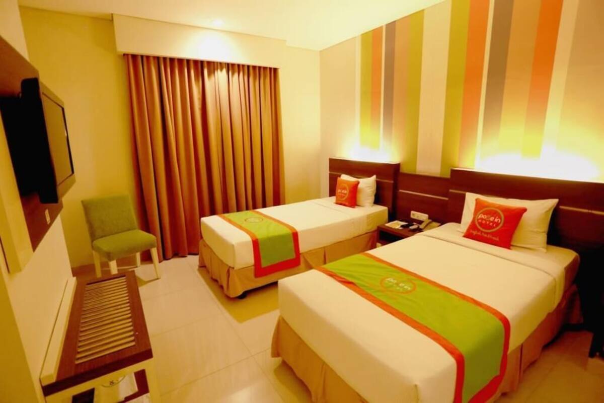A hotel room with two beds, a desk, a chair, and a TV.