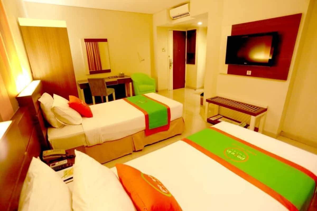 A hotel room with two beds, a desk, a chair, a TV, and a window.