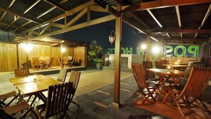 Un espacio de comedor al aire libre con mesas y sillas de madera, una zona de estar cubierta y un edificio con un letrero que dice "POLO".