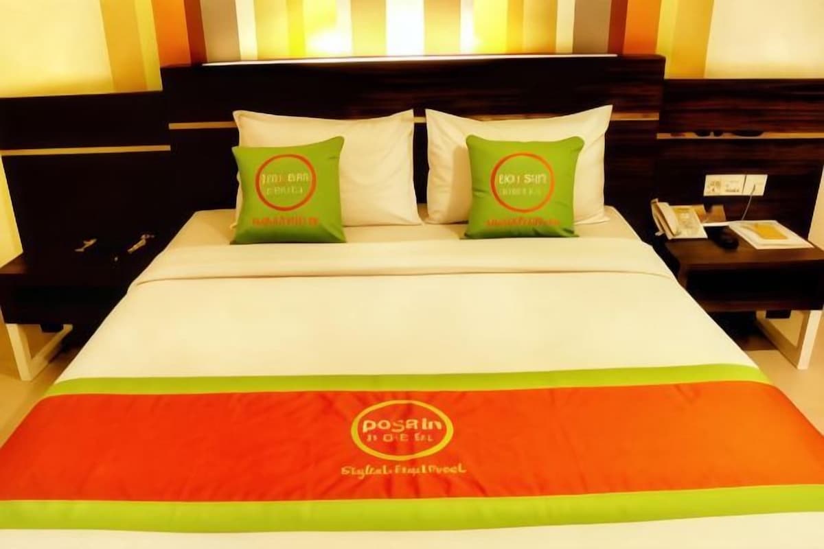 Una habitación de hotel con una cama, dos almohadas, una mesita de noche y una mesilla.