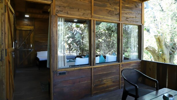 Una cabaña de madera con una cama, una ventana con vista a árboles y una mesa con un tazón.