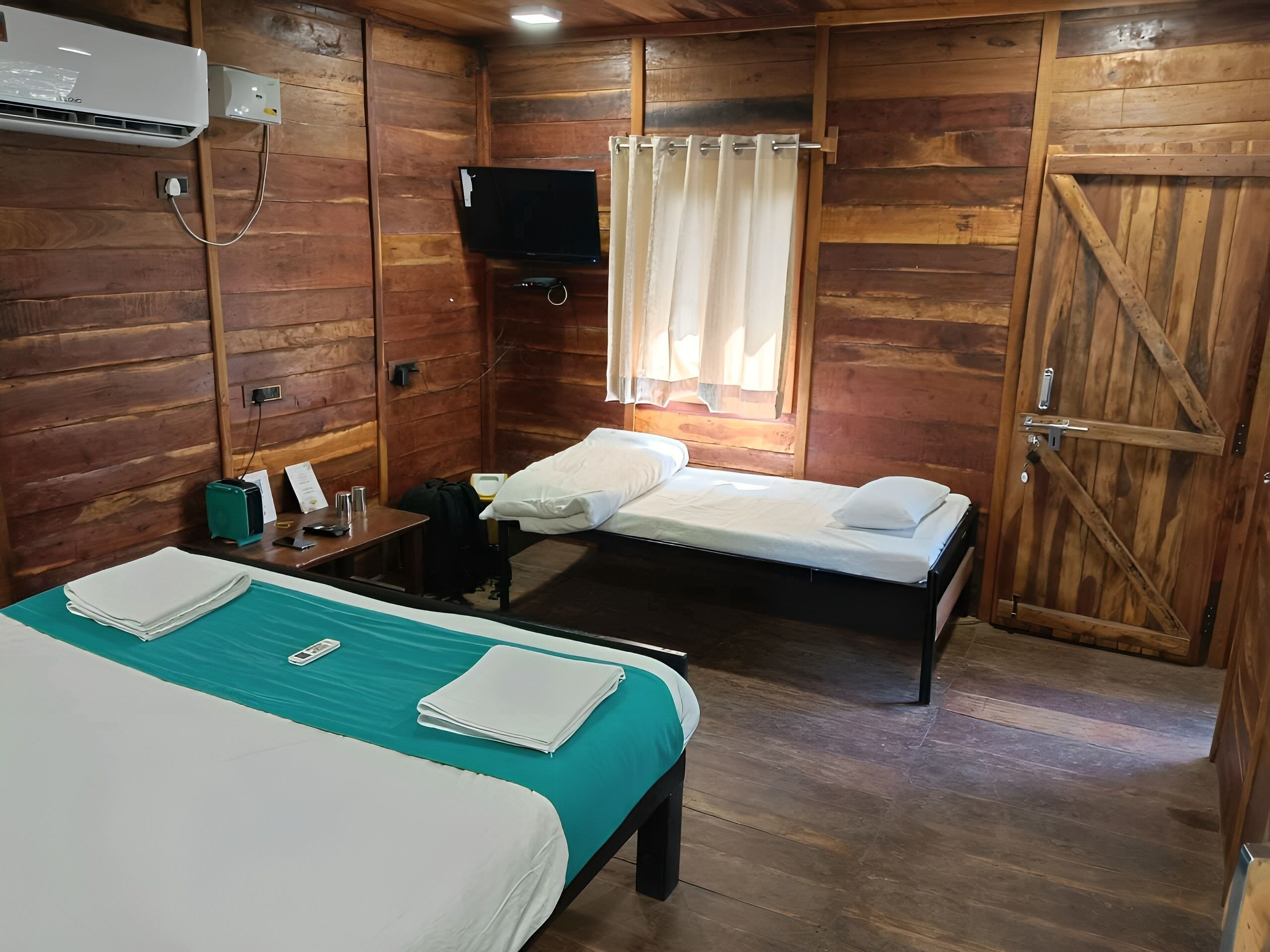 Una habitación estilo cabaña de madera con dos camas, un televisor y una ventana con cortinas.