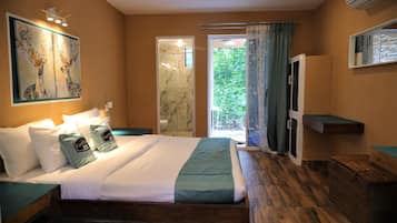 Camera da letto con un letto, un comodino, un quadro, una doccia e vista sul verde.