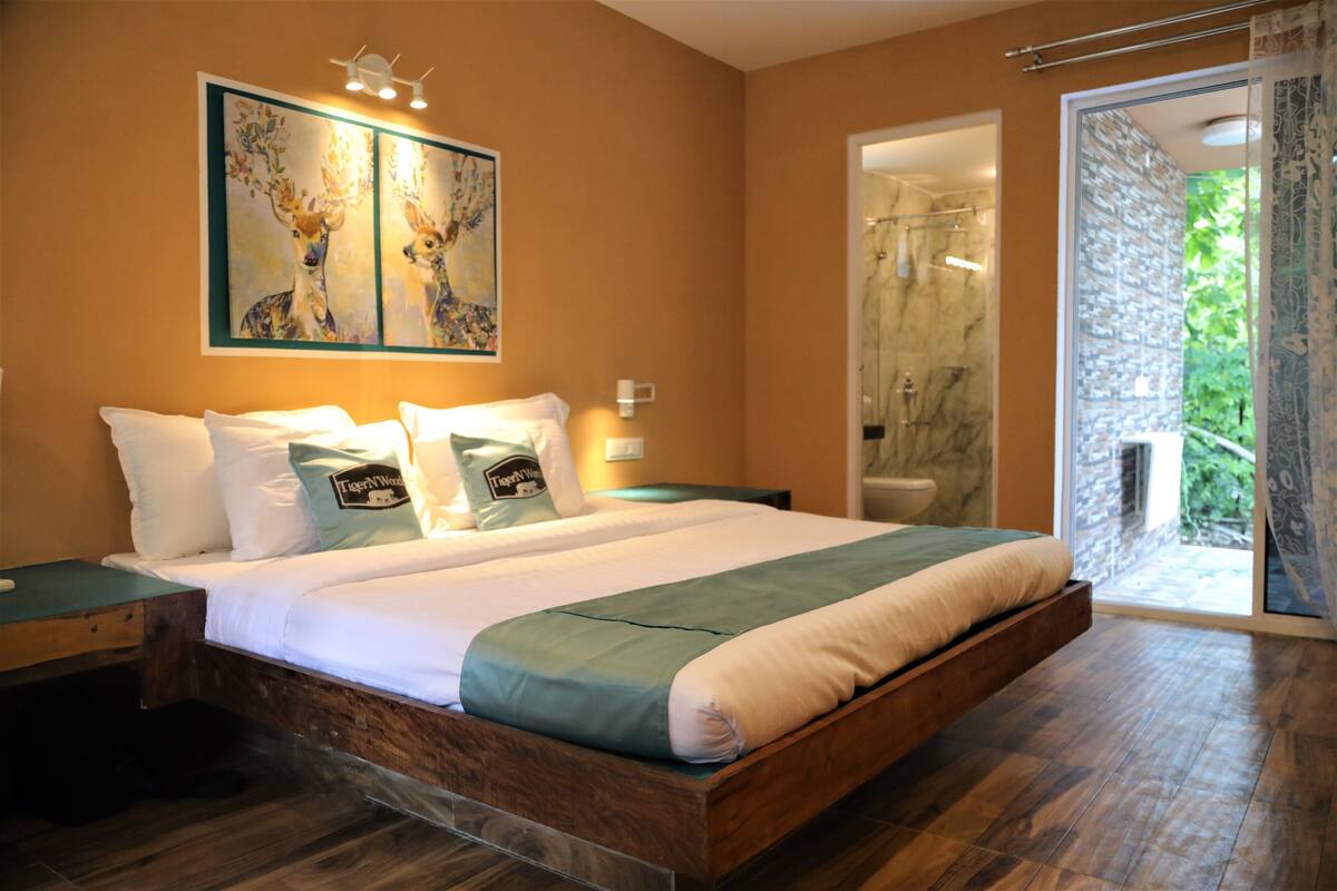 A bedroom with a large bed, a wooden headboard, a nightstand, a wall-mounted lamp, and a painting of deer.