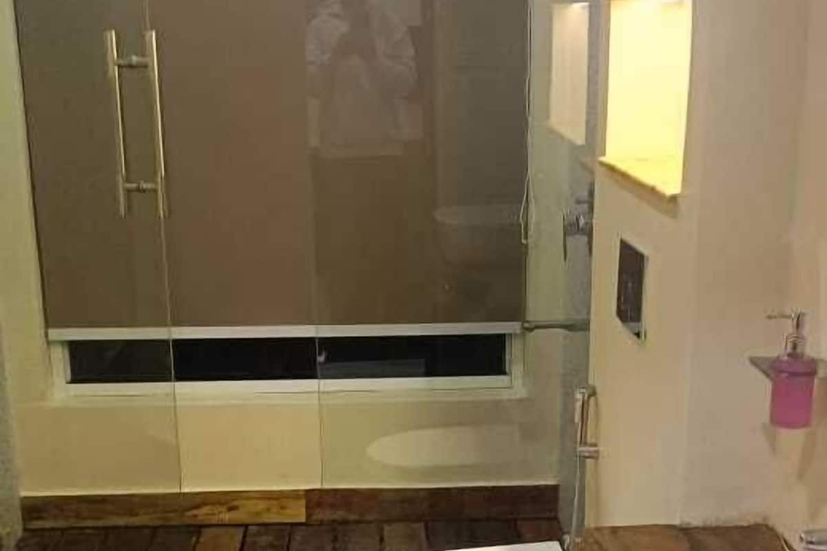 A bathroom with a wooden floor, a toilet, a sink, and a glass-enclosed shower area.