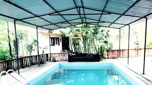 Piscina con zona cubierta, rodeada de plantas y una valla de madera.