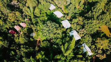 An aerial view of a campsite with several tents and a few cabins among dense forest.