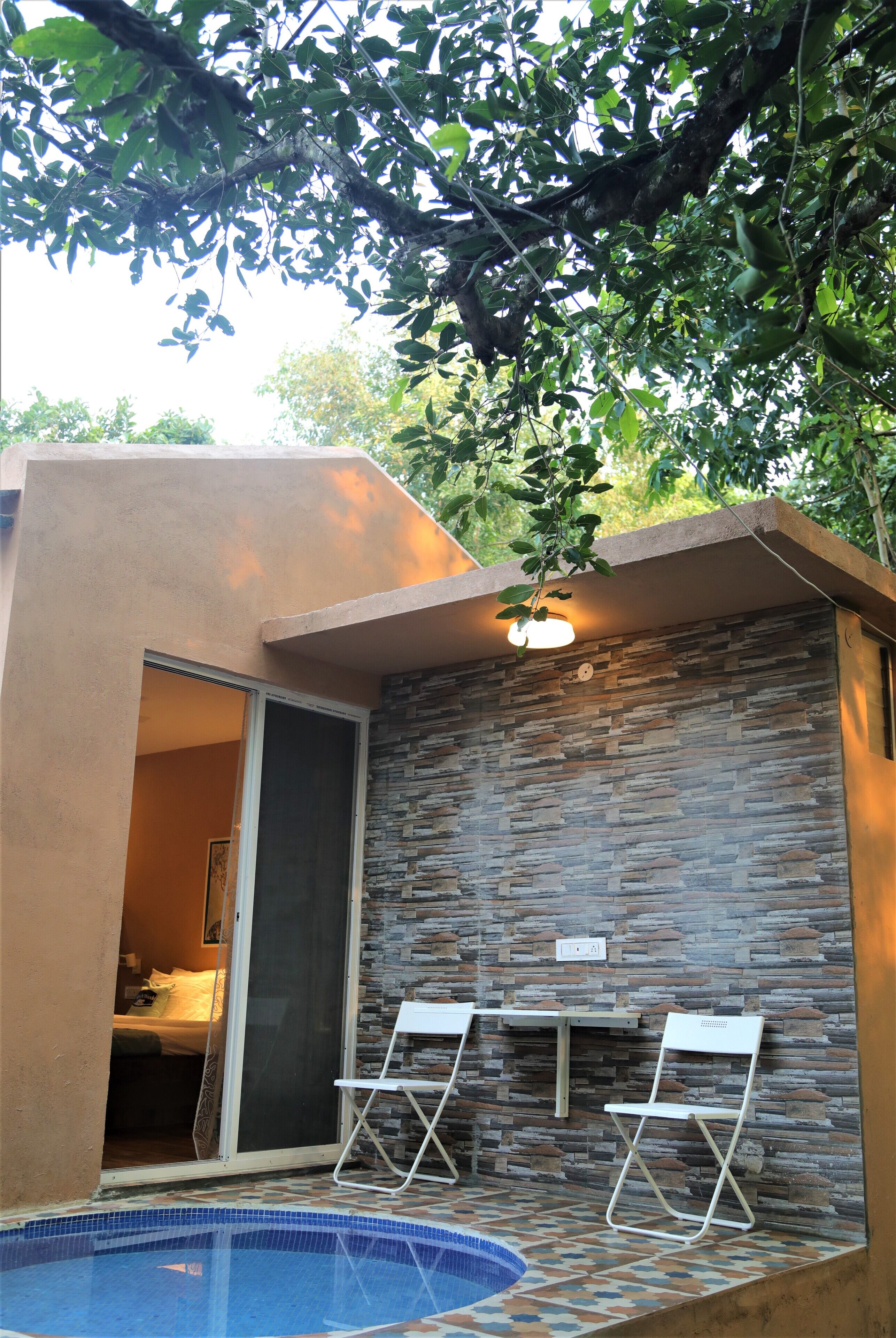 A modern outdoor area with a pool, two white folding chairs, and a stone wall.