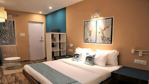 Habitación de hotel con una cama grande, una mesita de noche, una estantería, un cuadro decorativo en la pared y un baño con ducha e inodoro.