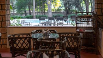 Un patio con mobiliario de mimbre, una pequeña mesa con cubierta de vidrio y vistas a una piscina y follaje.
