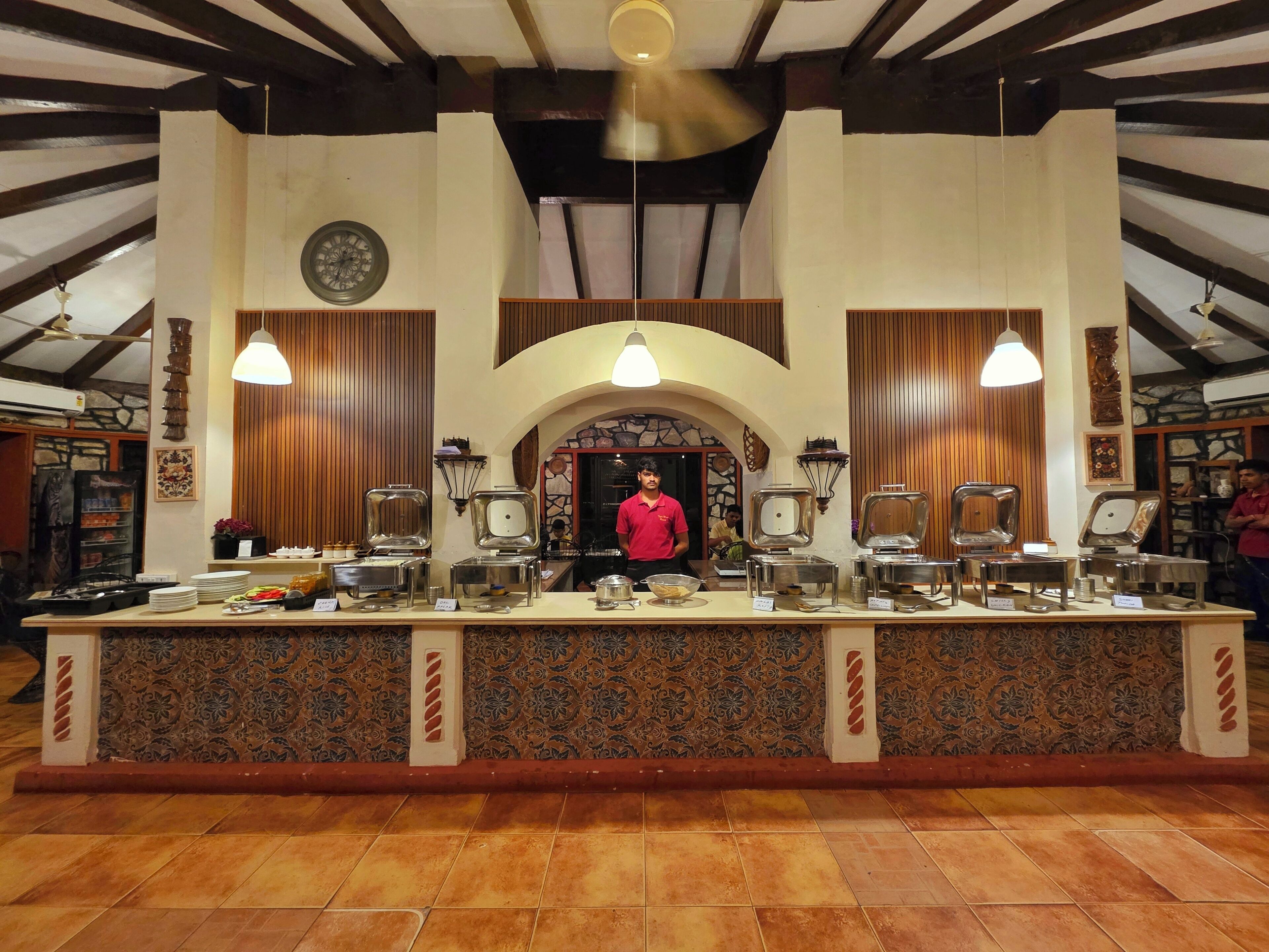 Zona de bufé con una mesa de servicio central, varias estaciones de comida y una persona de pie detrás.