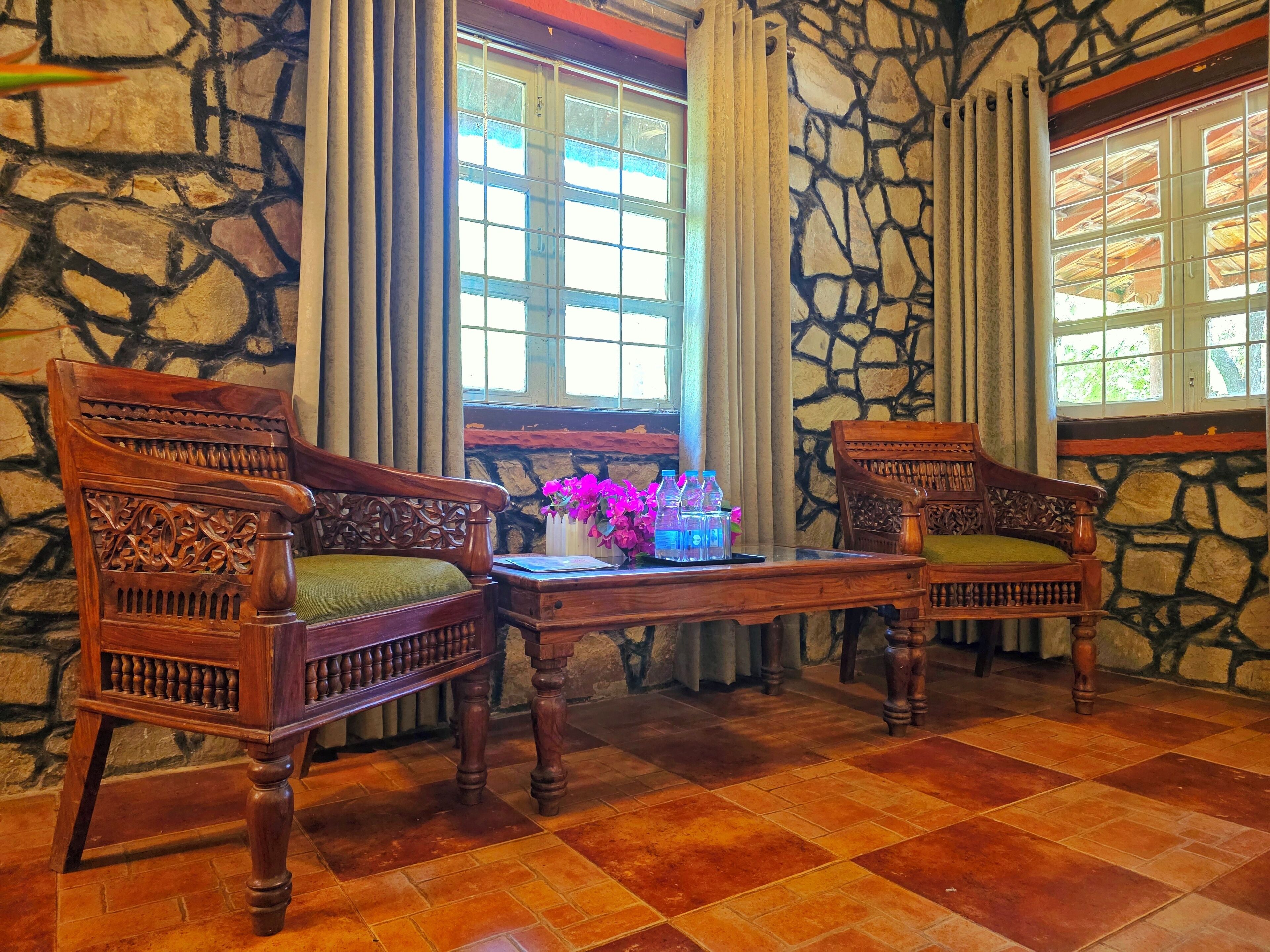 A room with two wooden chairs, a small table with a vase of flowers, and a window with curtains.