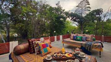 A terrace with two beds, a dining table with breakfast, and a view of trees.
