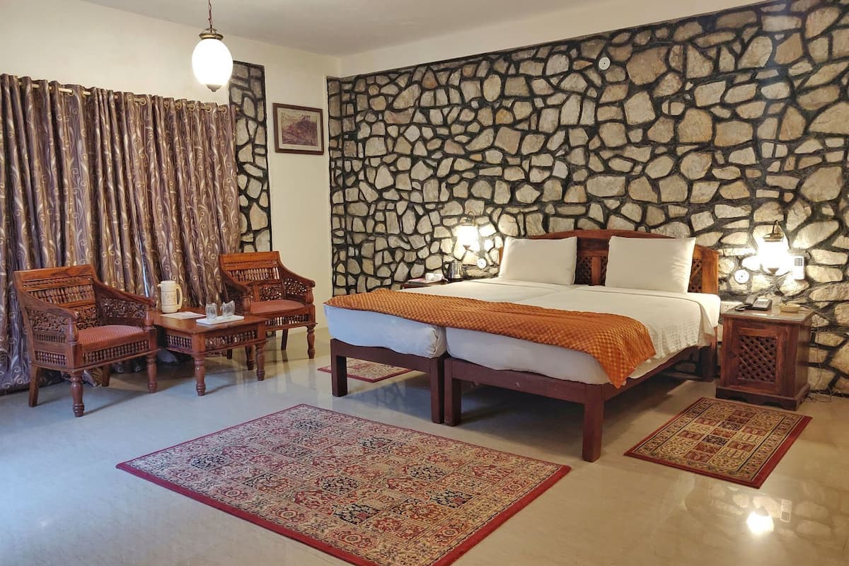 Een kamer met een stenen muur, een bed, twee stoelen, een tafel en twee tapijten.