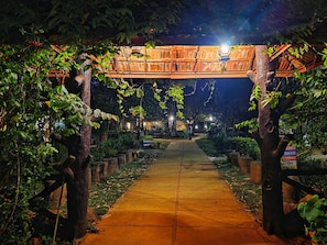 A pathway leading to a reception area under a wooden archway, surrounded by greenery and illuminated by overhead lights. - Tiger Moon Resort (Sawai Madhopur)