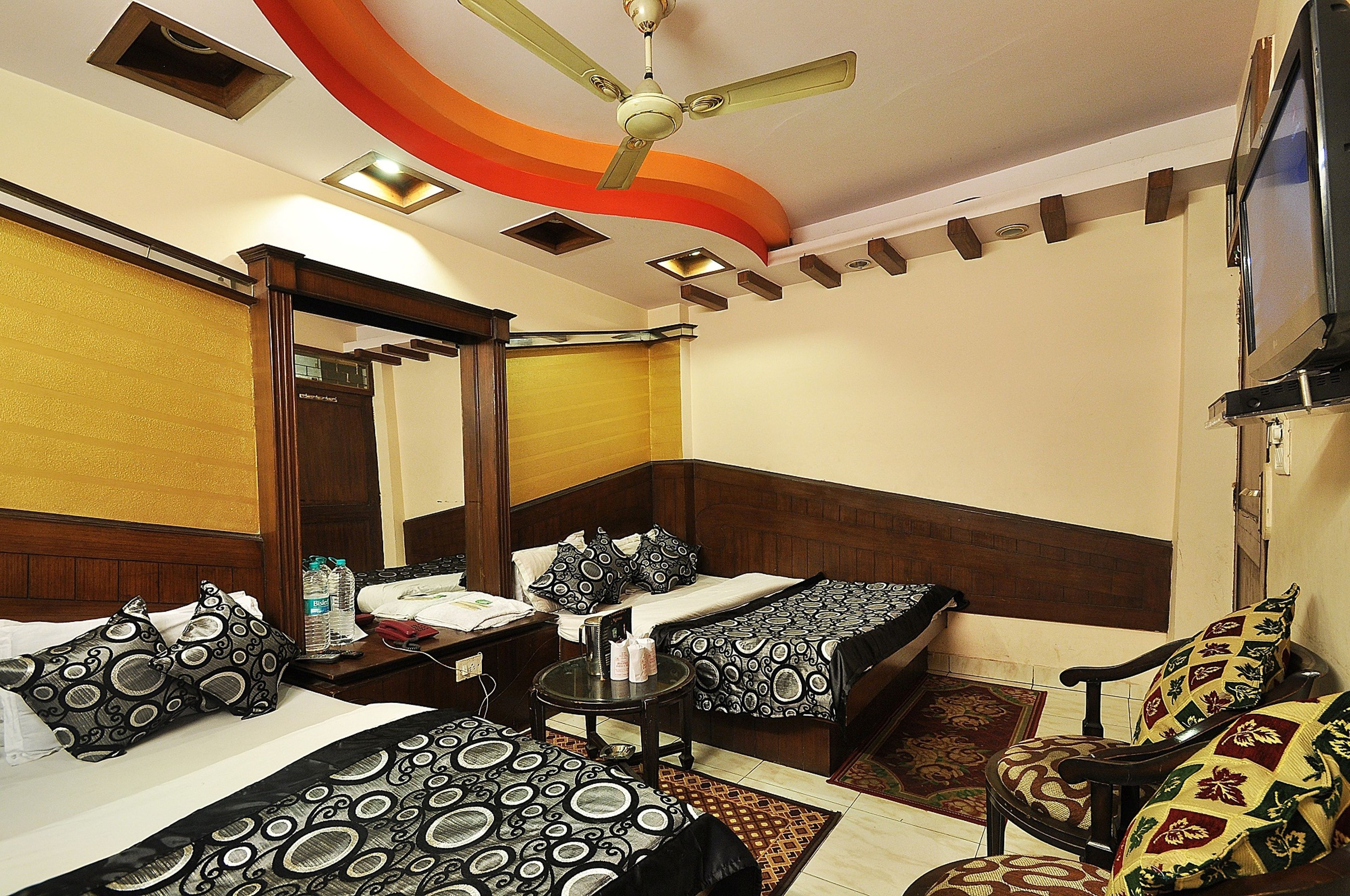 A hotel room with two beds, a ceiling fan, a TV, and a small table with a chair.