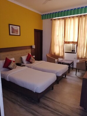 Une chambre d’hôtel avec deux lits, une petite table, une chaise, un ventilateur de plafond et une fenêtre avec des rideaux.