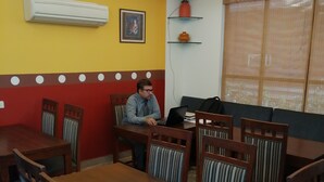 Un espace repas avec des tables et des chaises en bois, un ventilateur de plafond et une fenêtre équipée de stores.