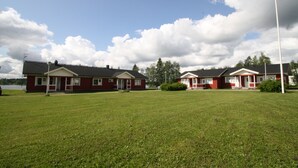 Een rij rode huizen met witte details, een gazon en een waterpartij op de achtergrond.