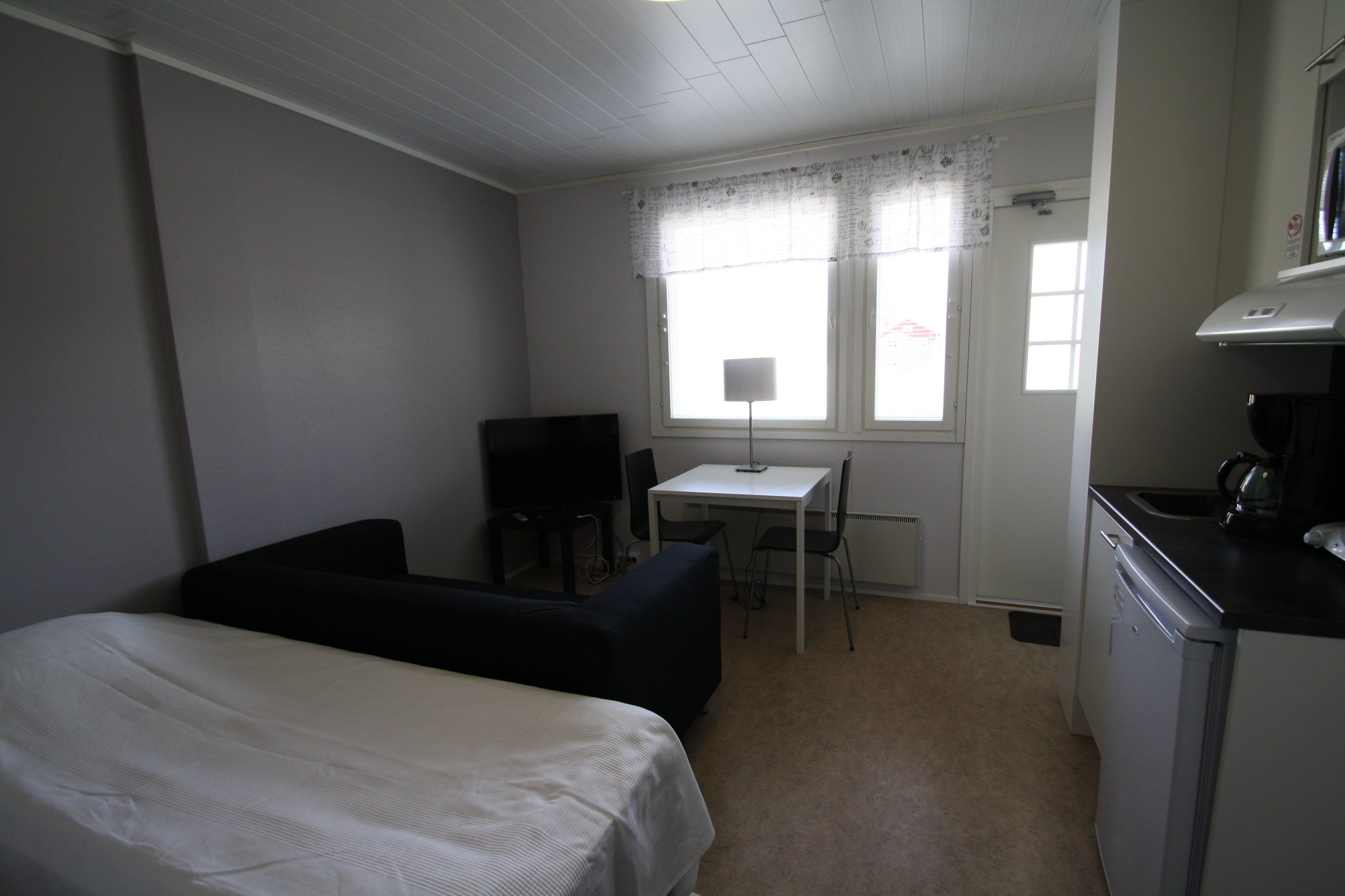 A small, compact room with a bed, a desk, a chair, and a kitchenette.
