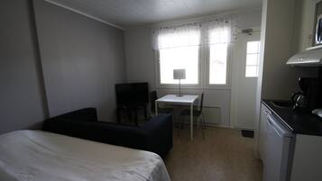 A small, compact room with a bed, a desk, a chair, and a kitchenette.
