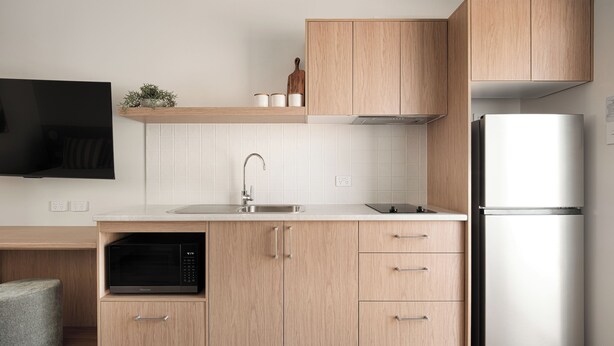 A modern kitchen with wooden cabinets, a built-in microwave, a stainless steel sink, and a white refrigerator. - Catalina Motel Lake Macquarie (Toronto)