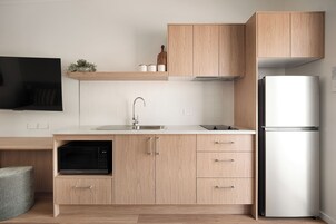 A modern kitchen with wooden cabinets, a built-in microwave, a stainless steel sink, and a white refrigerator.