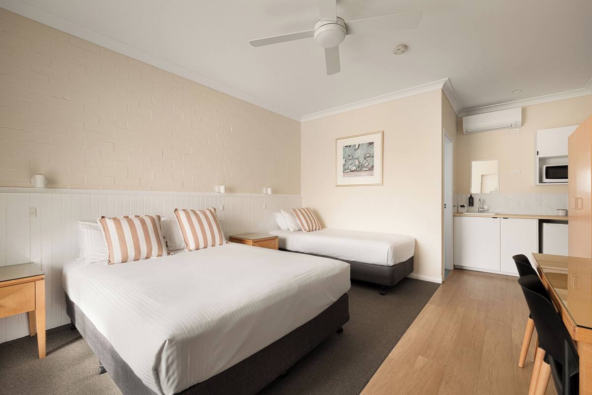 Een slaapkamer met twee bedden, een bureau, een stoel, een eettafel en een kitchenette.