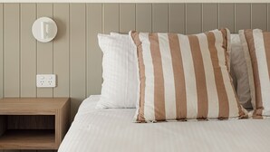 A bed with striped pillows, a bedside table, and a wall-mounted light fixture. - Catalina Motel Lake Macquarie (Toronto)