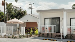 A modern two-story building with a white exterior, a wooden front door, and a number '25' on the side. - Catalina Motel Lake Macquarie (Toronto)