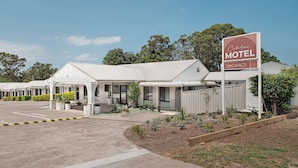 A motel with a sign indicating vacancy, a parking lot, and a landscaped area with plants. - Catalina Motel Lake Macquarie (Toronto)