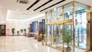 Een moderne lobby met glazen entree, een zithoek en potplanten.