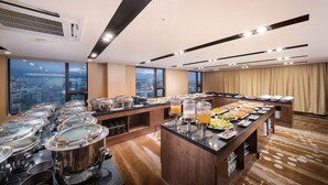 Een buffetopstelling met diverse gerechten en drankjes, een groot raam met uitzicht over de stad, en een modern interieur.