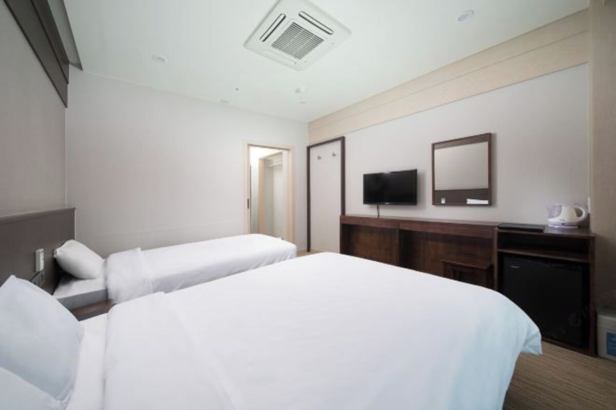 Habitación de hotel con dos camas individuales, televisión, escritorio con silla y cafetera.