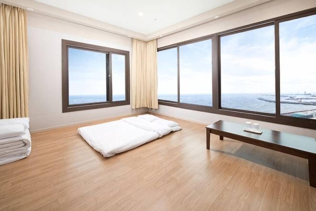 Una habitación de hotel con un ventanal grande, una cama, una mesita de noche y una pila de toallas.