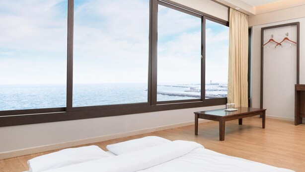 Een hotelkamer met een groot raam met uitzicht op zee, een bed, een klein tafeltje en een kapstok.
