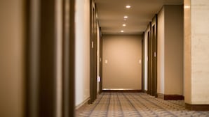 Een hotelgangen met een kamerbreed tapijt, inbouwverlichting en een effen muur.