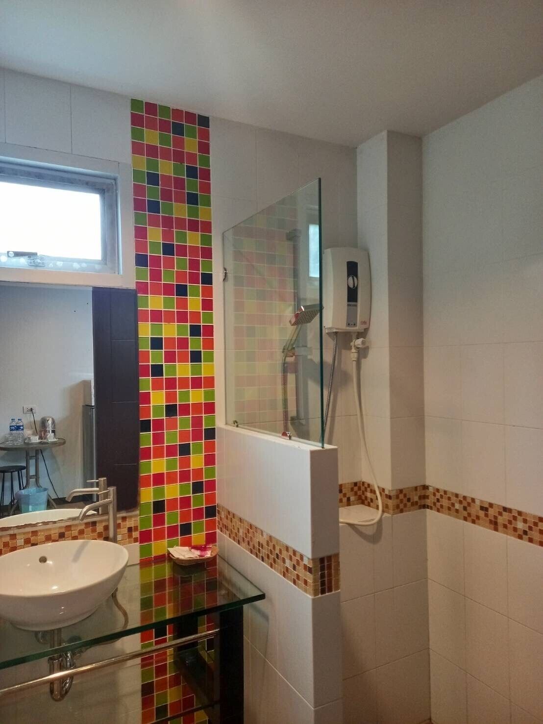 Un baño con pared de mosaicos de colores, un lavabo de vidrio, un espejo y una ducha con cabezal de ducha manual.