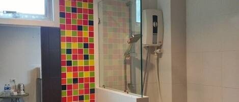 A bathroom with a colorful mosaic tile wall, a glass sink, a mirror, and a shower with a handheld showerhead.