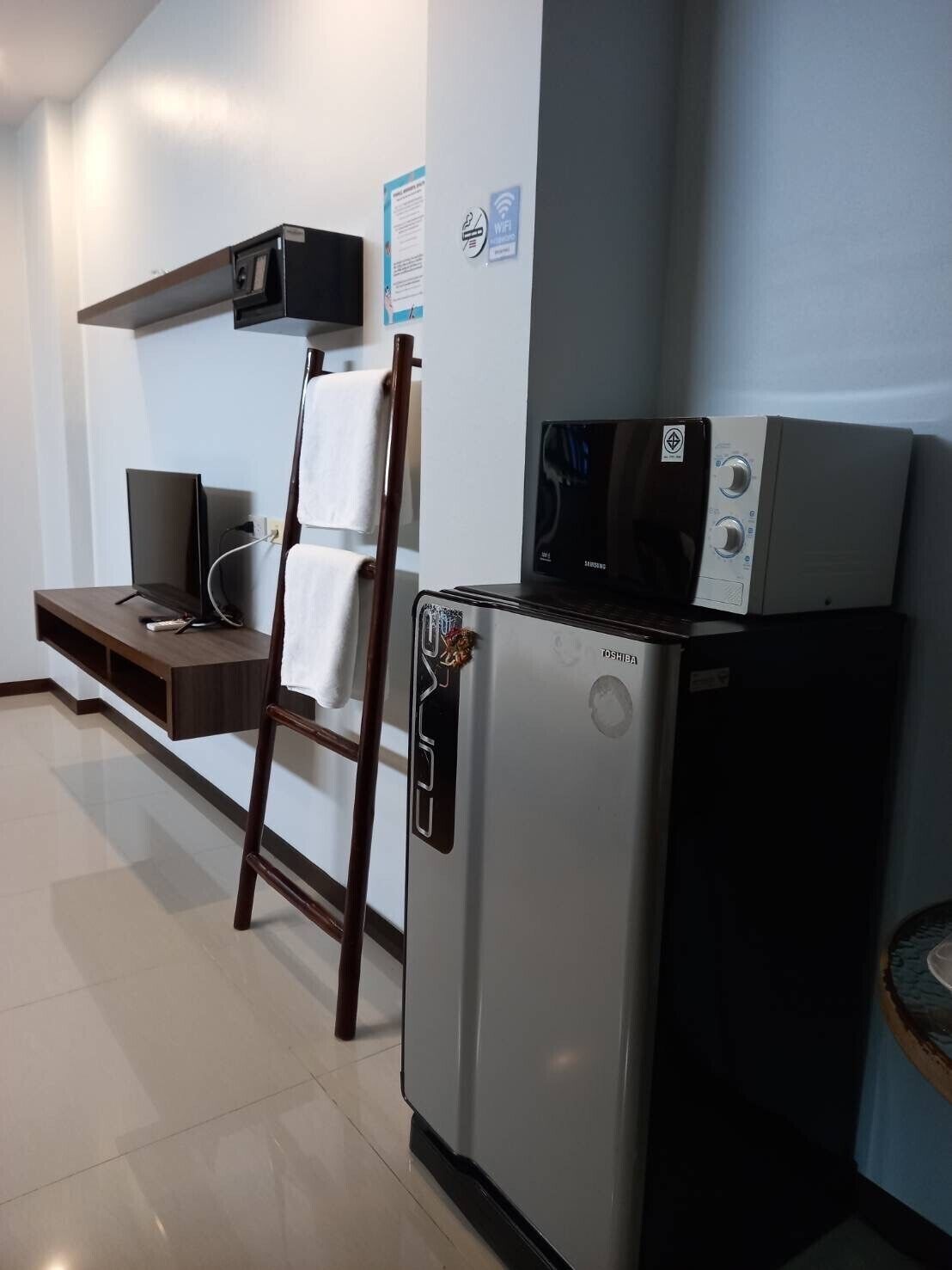 Una kitchenette compacta con refrigerador, microondas y un televisor pequeño.