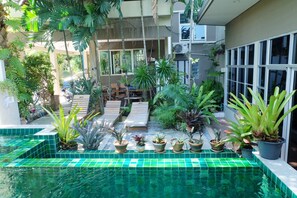 A pool area with tiled flooring, lounge chairs, and various potted plants.