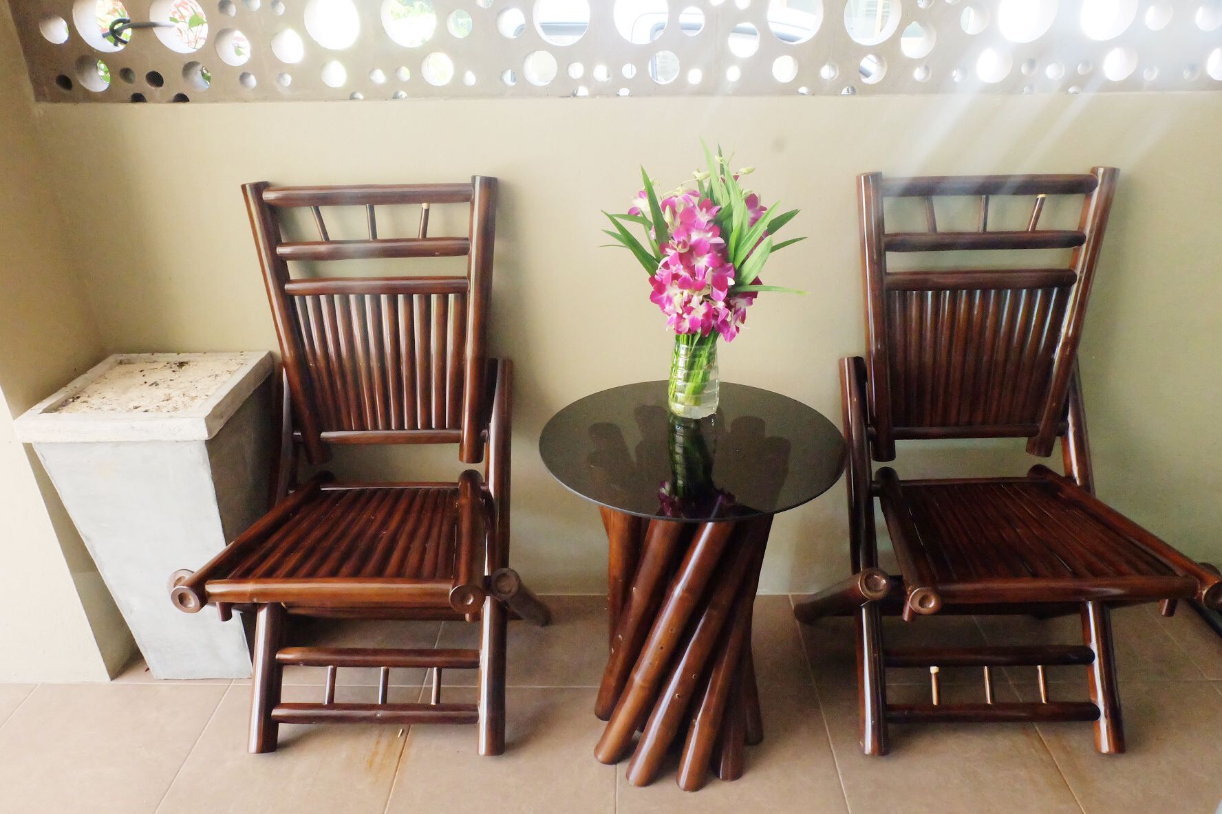 Two wooden chairs with a glass table and a vase of flowers between them.