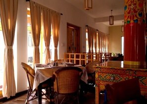 A dining area with a long table, chairs, and curtains. - Saboo Resorts (Leh)