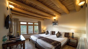 Habitación de hotel con dos camas, suelo de madera, un ventanal grande y techo con vigas a la vista.