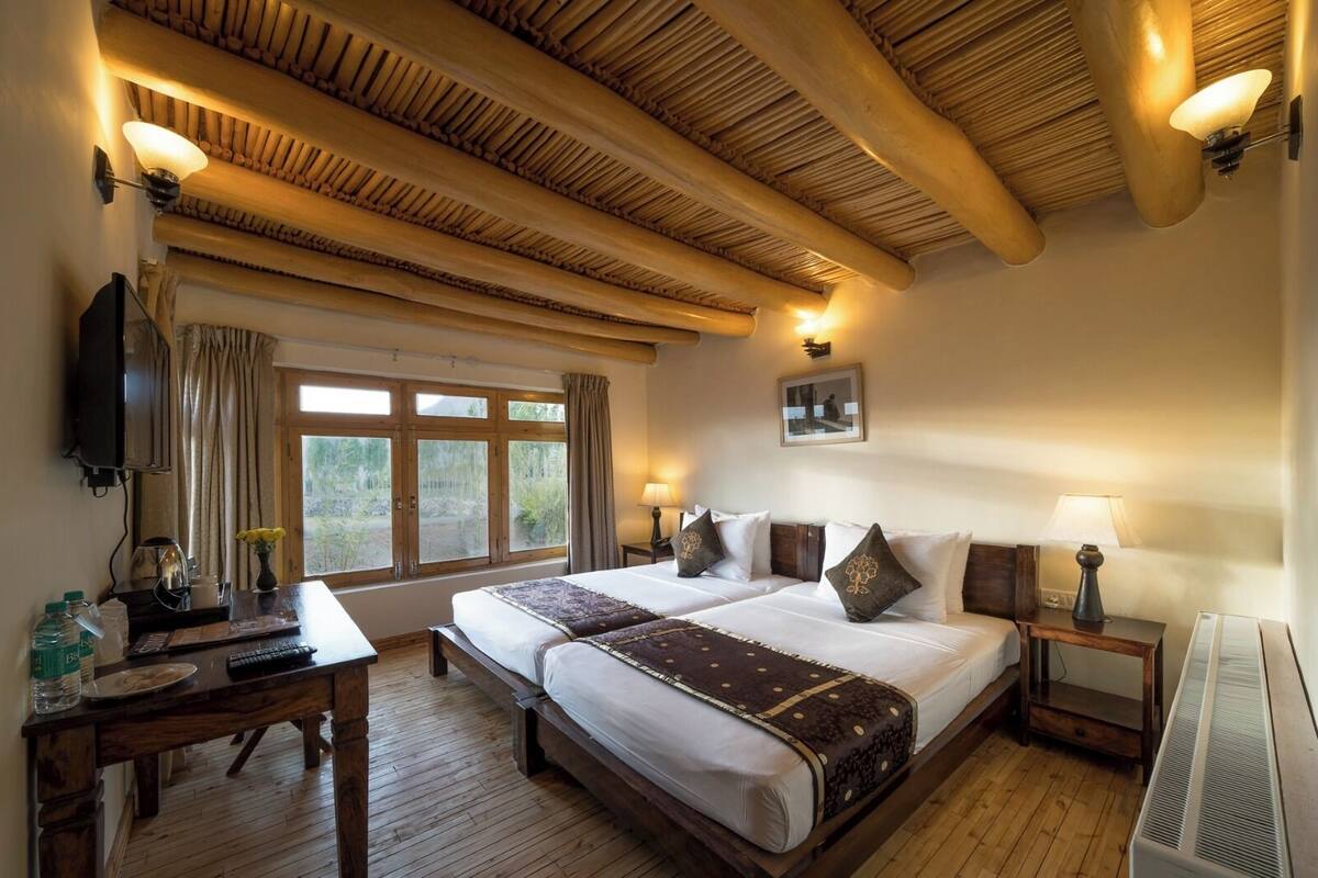 A hotel room with two beds, wooden flooring, a large window, and a ceiling with exposed beams.