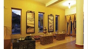 Una habitación con suelo de madera, un mueble de madera oscuro con intrincados grabados, un ventanal con vistas a las montañas y una pared decorada con cuadros.