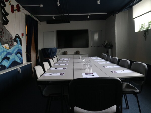Un salón de conferencias con una larga mesa, sillas, una pantalla de proyector y un mural en la pared.