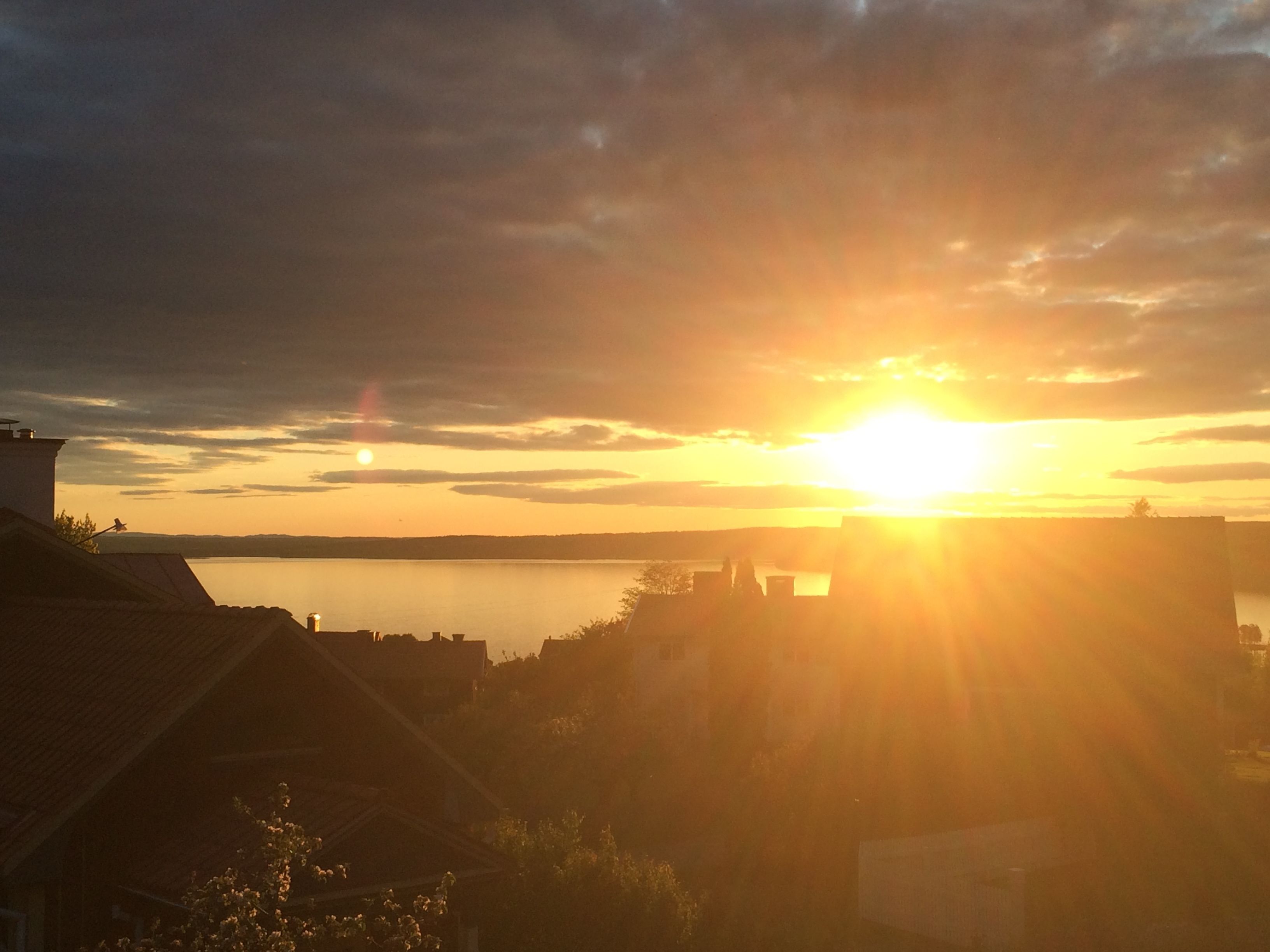 Solnedgang over vand med silhuetter af bygninger mod himlen.