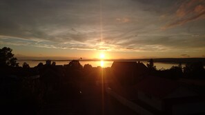 Ein Sonnenuntergang über einem Gewässer, im Vordergrund Gebäude.